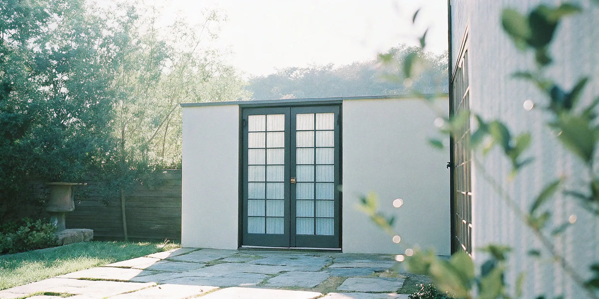 Black exterior French doors with built-in blinds opening onto a modern patio.