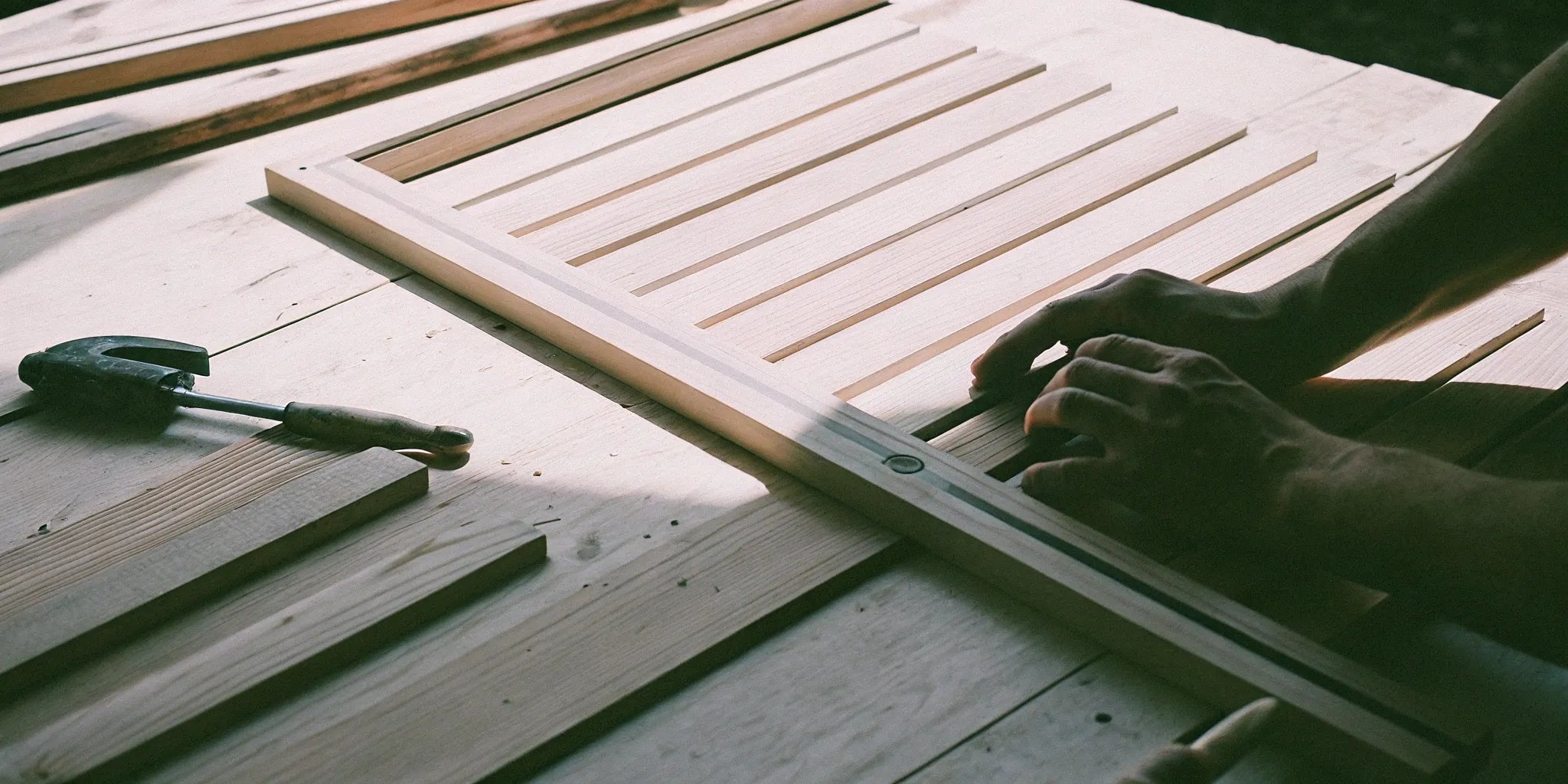 A person assembling a wood slat acoustic panel on a workbench.