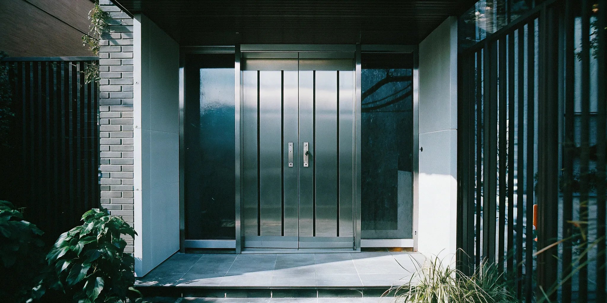 Modern stainless steel entry doors with a sleek, minimalist design and long vertical handles.