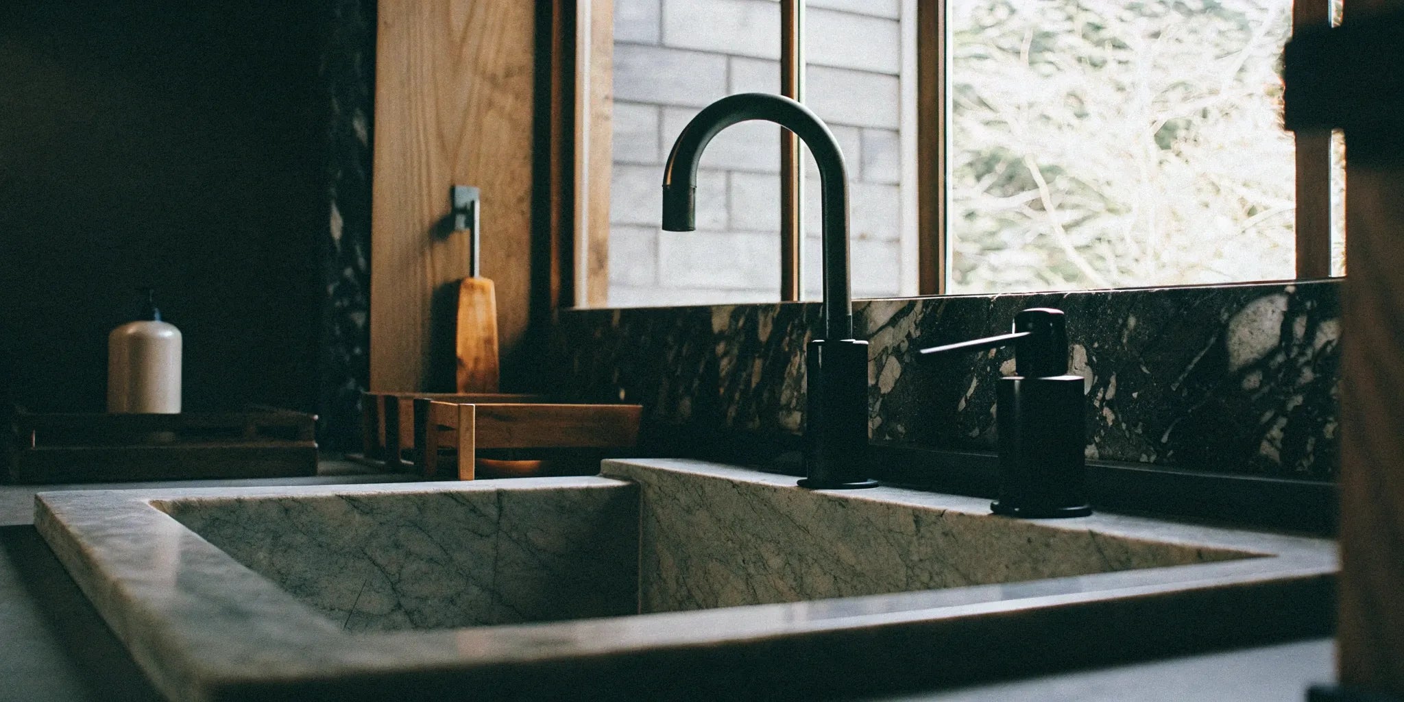 Matte black bathroom fixtures, including a faucet and soap dispenser, on a marble sink.
