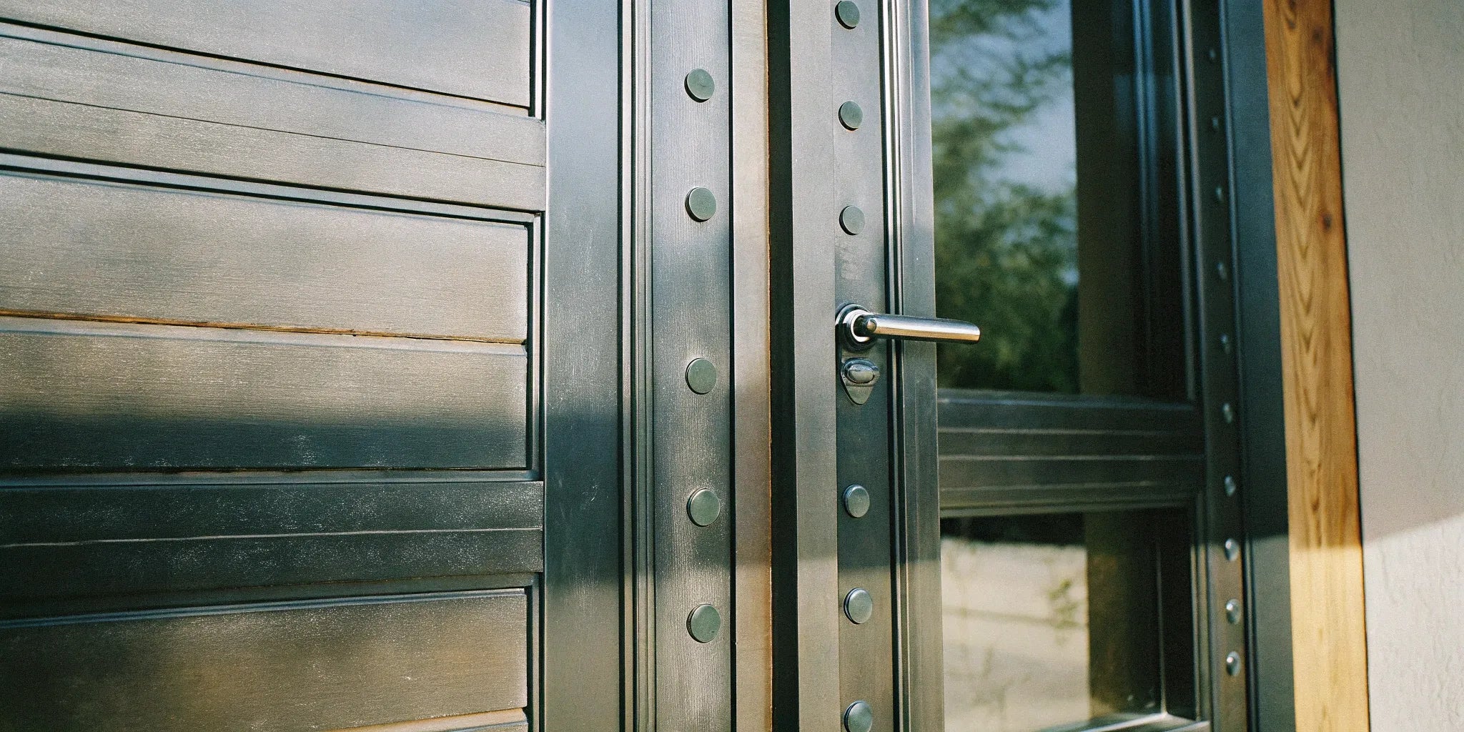 A modern custom steel exterior door with a long pull handle and rivet details.