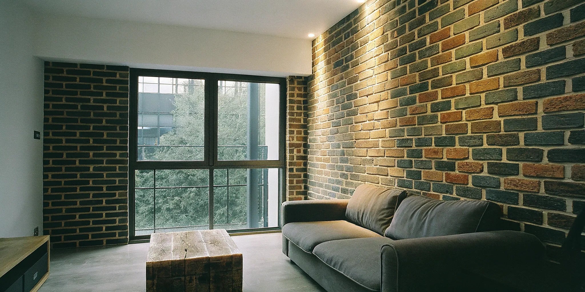 Modern living room interior with a faux brick wall panel accent wall behind a gray sofa.