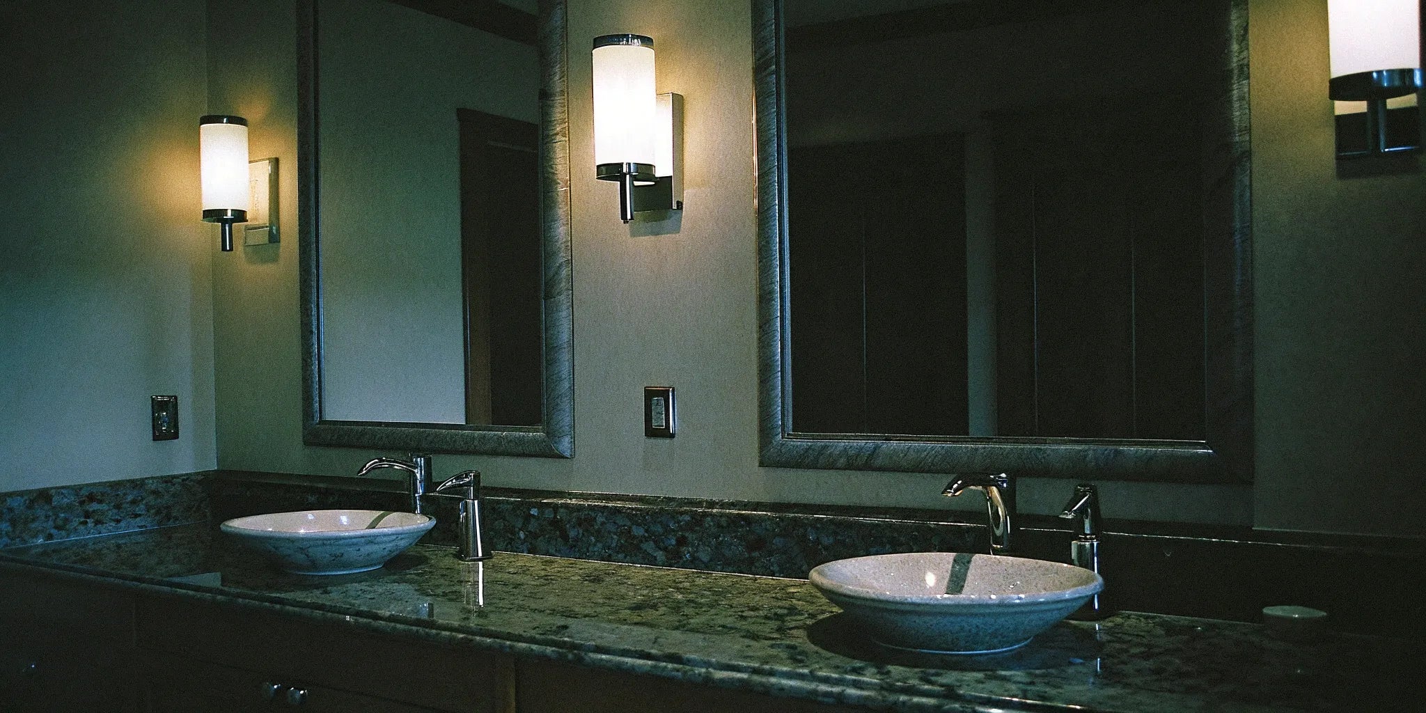 Modern bathroom vanity lighting installed over a double sink with a granite countertop.