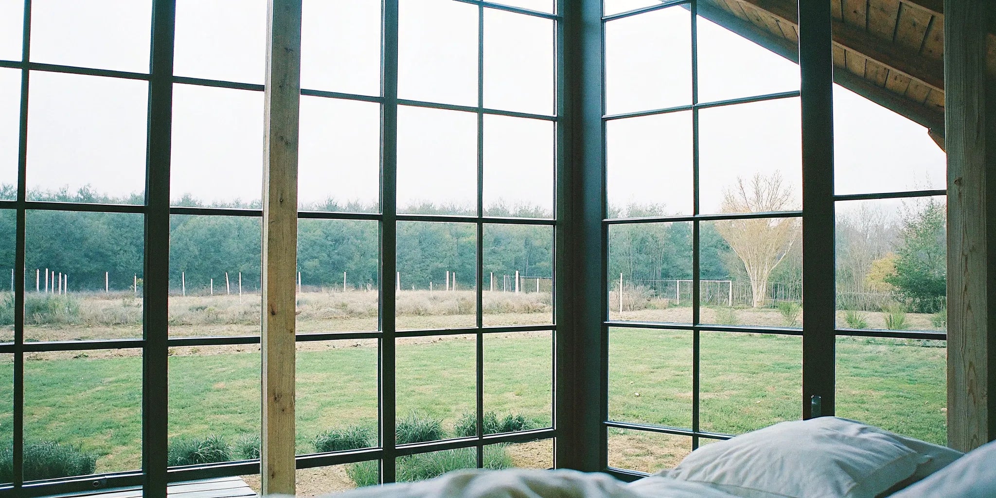 Interior of a modern farmhouse with large black steel windows overlooking a green yard.