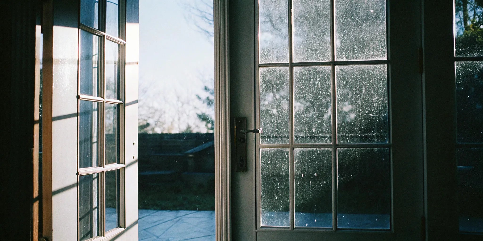 A pair of outswing French doors with glass panels opening onto a sunlit patio.